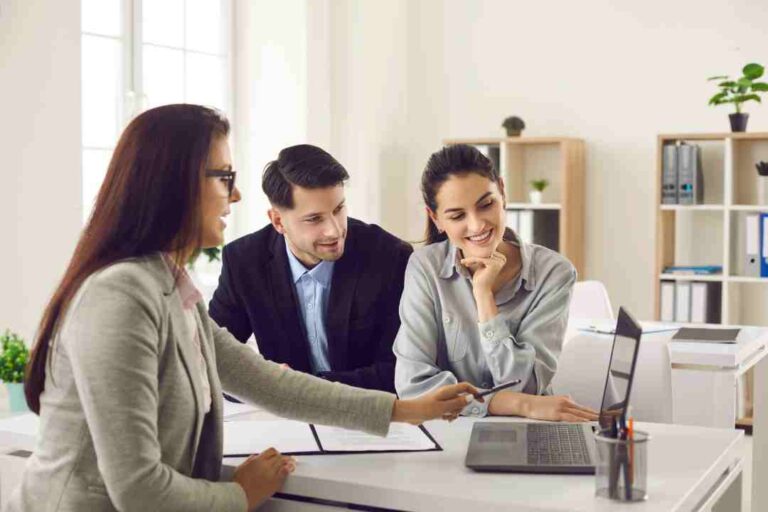 Real estate agent showing a laptop to a smiling couple, discussing property.